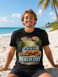 Man wearing a black t-shirt with a beach-themed design on a sandy beach.